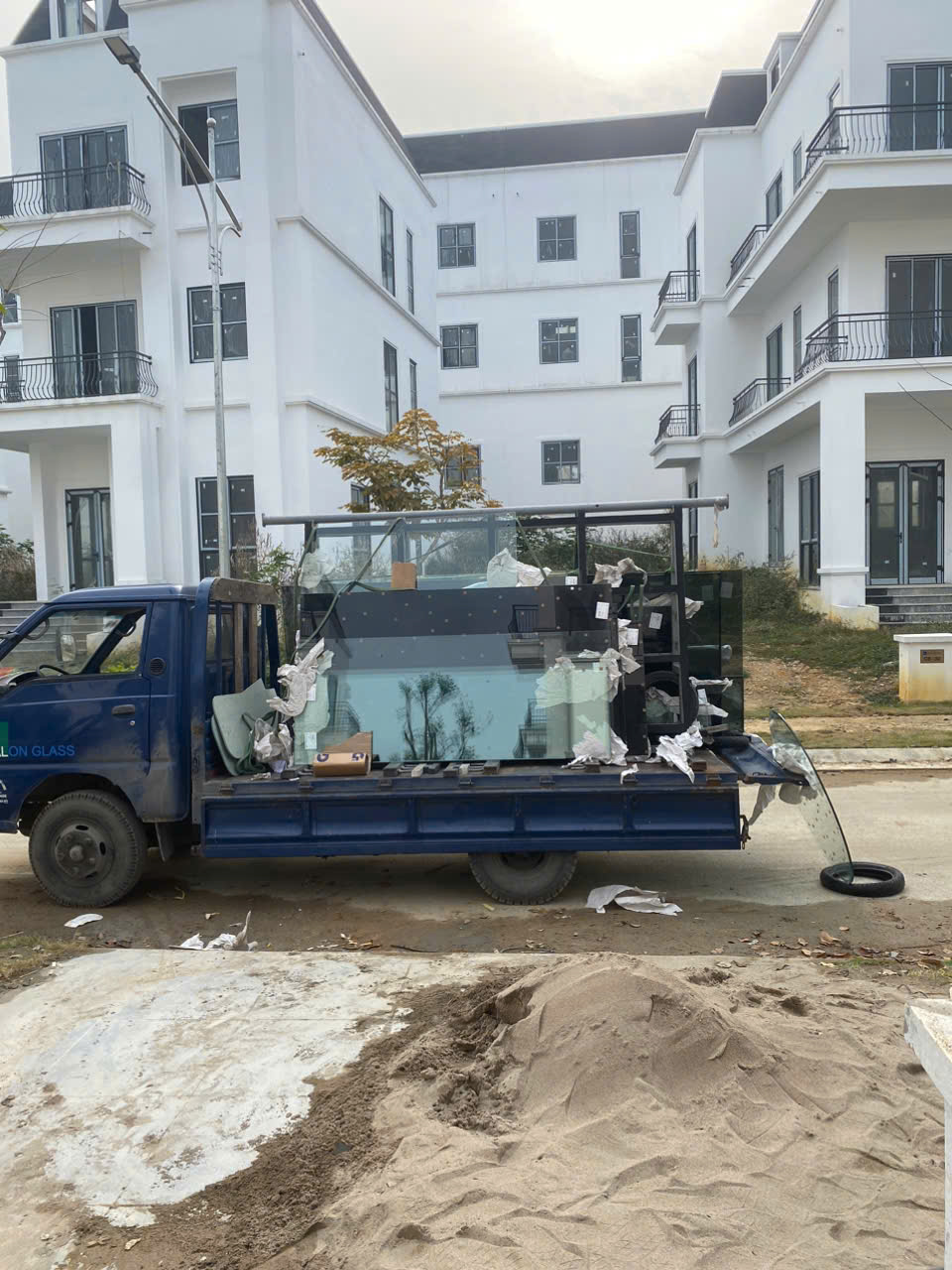 Xe tải chở kính cường lực và phụ kiện thi công đỗ trước dãy nhà đang xây dựng